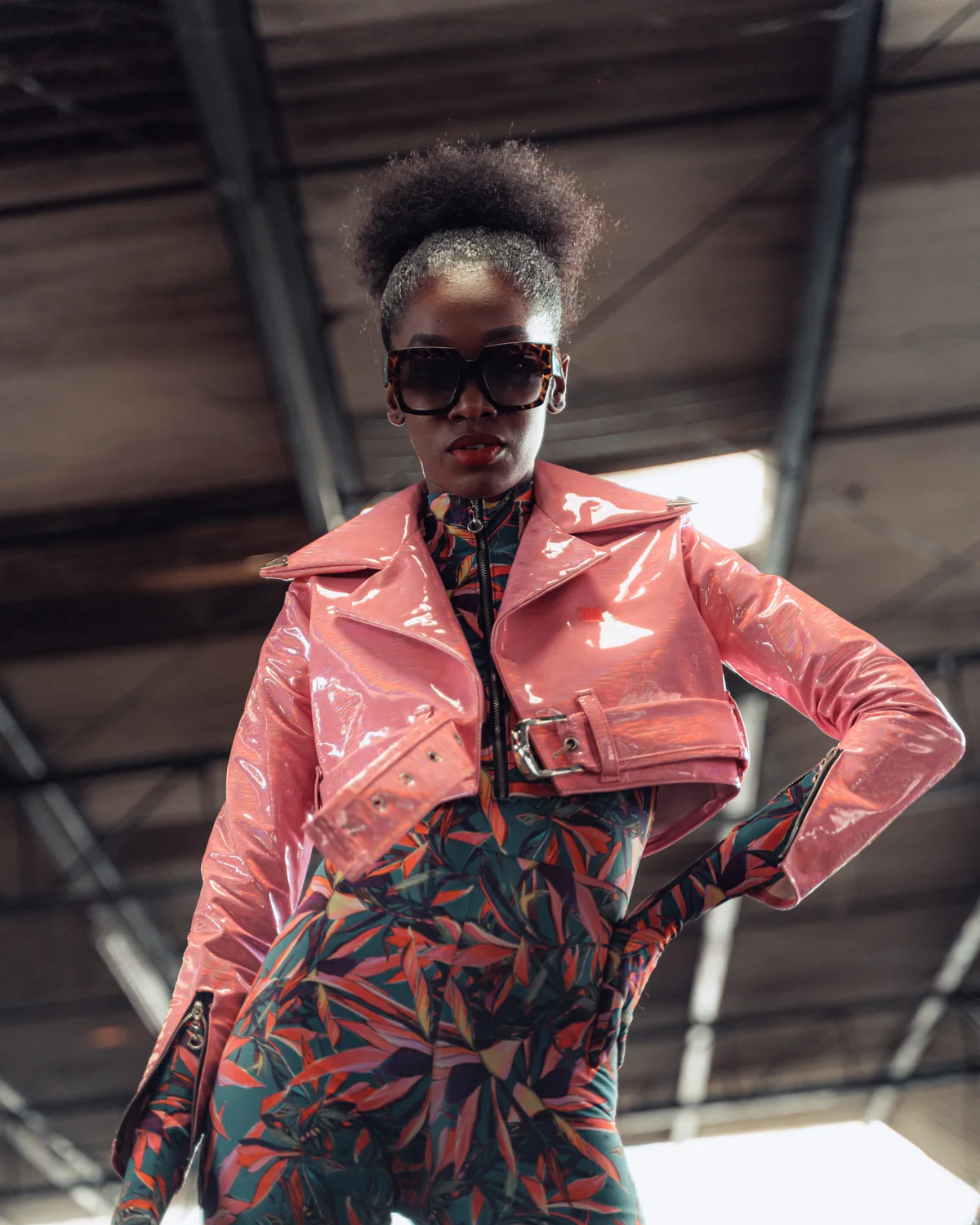 Daha Garcés con chaqueta rosada de charol y enterizo estampado, foto editorial en una galería de mercado