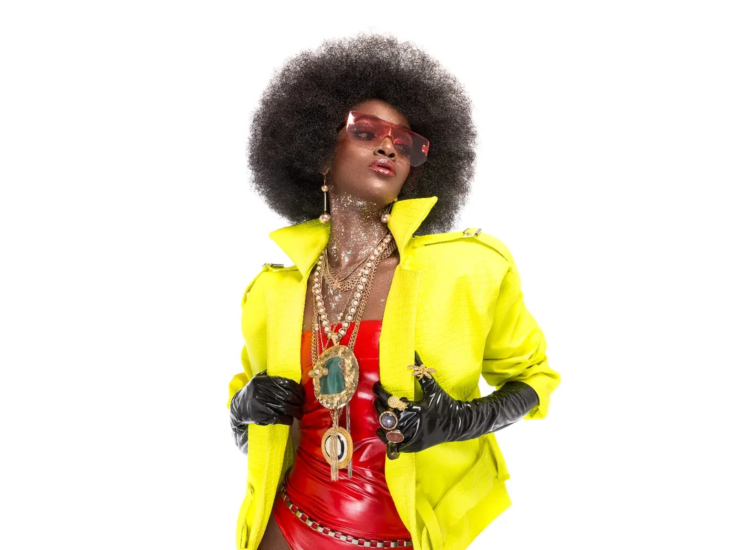 Daha Garcés con chaqueta amarilla, gafas rojas, collares dorados y guantes negros, foto editorial