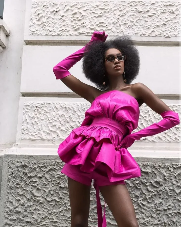 Modelo con vestido y guantes fucsia posando frente a una fachada blanca