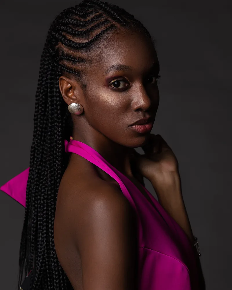 Retrato de una modelo con trenzas largas y vestido fucsia, mirando por encima del hombro